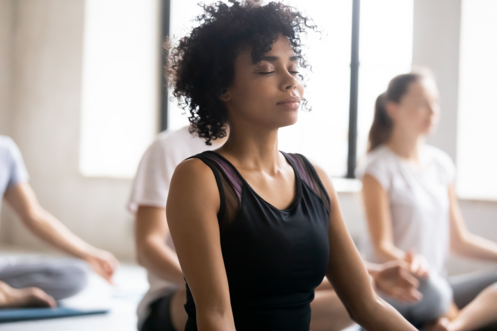 Concept of yoga class, focus on the closed eyes of African women of mixed race do meditation practice with partners during the session. No stress, reducing fatigue after sports exercise, wellness.