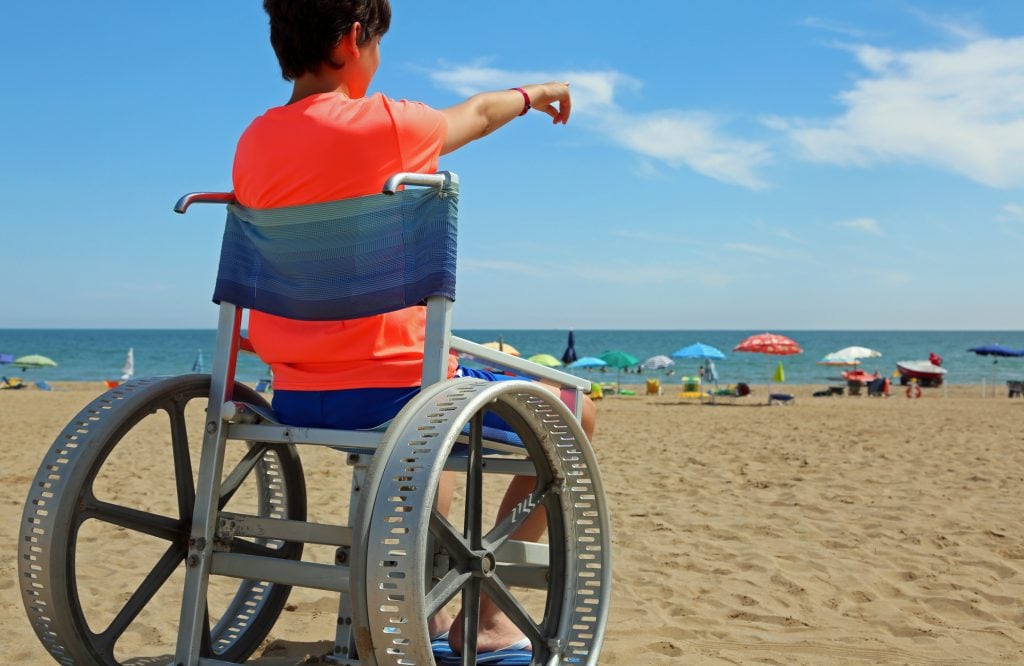 Niño en una silla de ruedas apuntando hacia el horizonte del mar en la playa en verano
