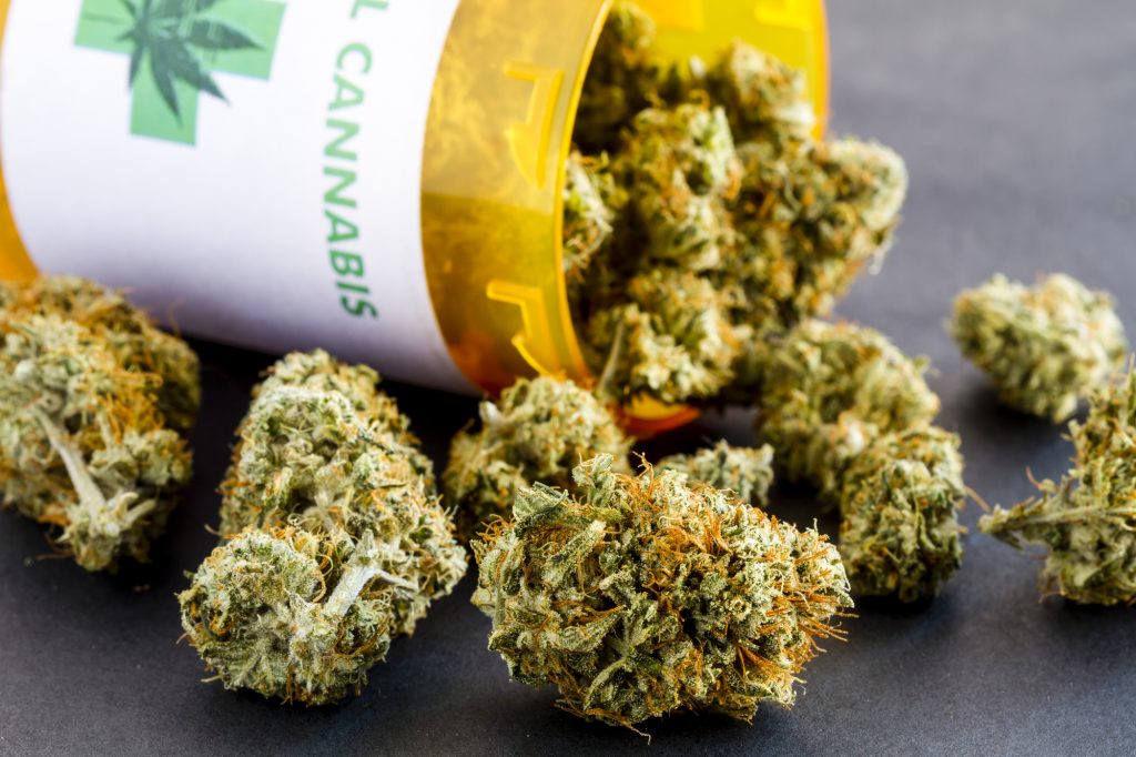 Primer plano de los cogollos de marihuana medicinal que se derraman fuera de la botella de la prescripción con la etiqueta en el fondo negro